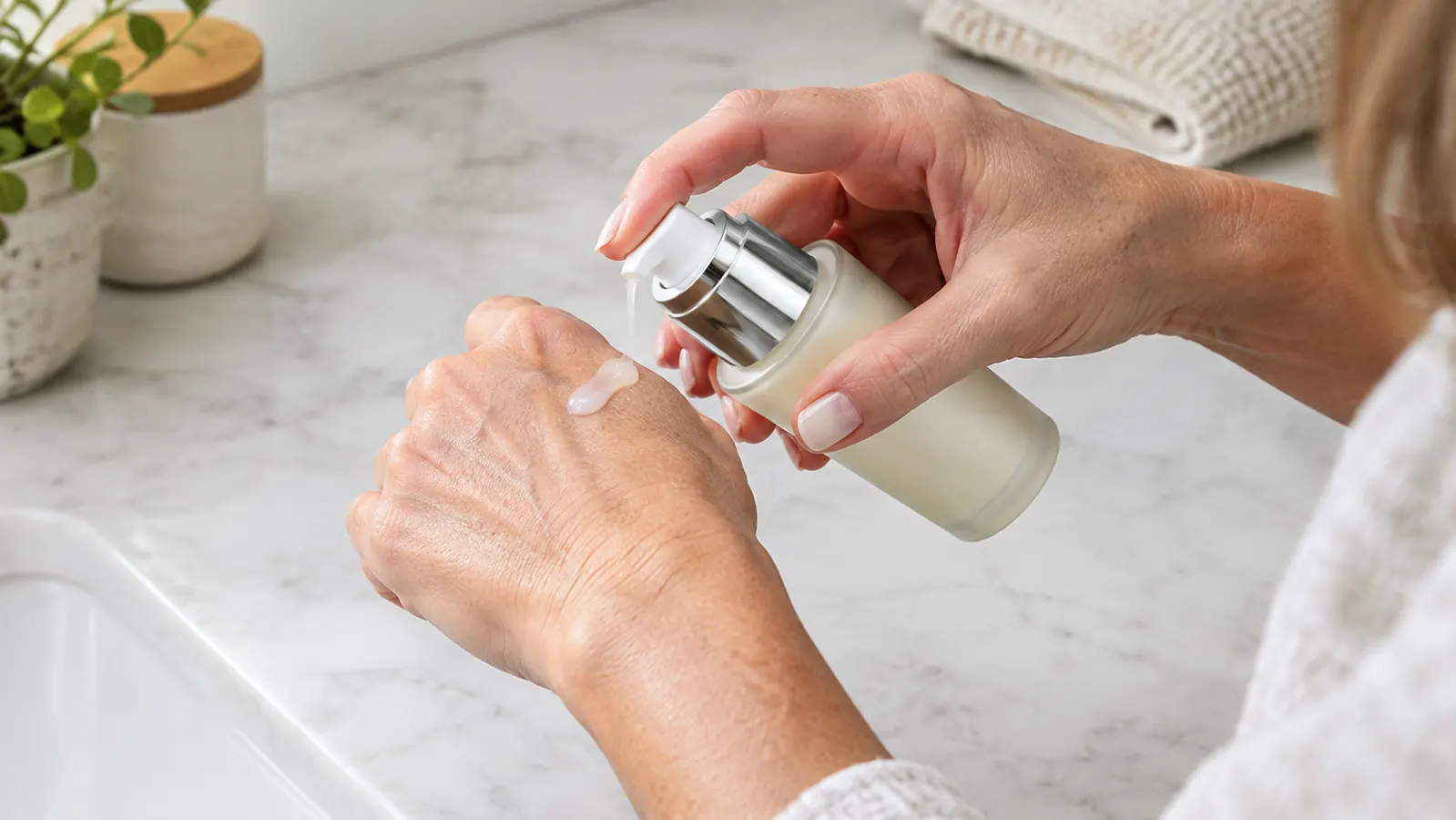 A hand holding a small bottle of lotion-like serum over a bathroom counter