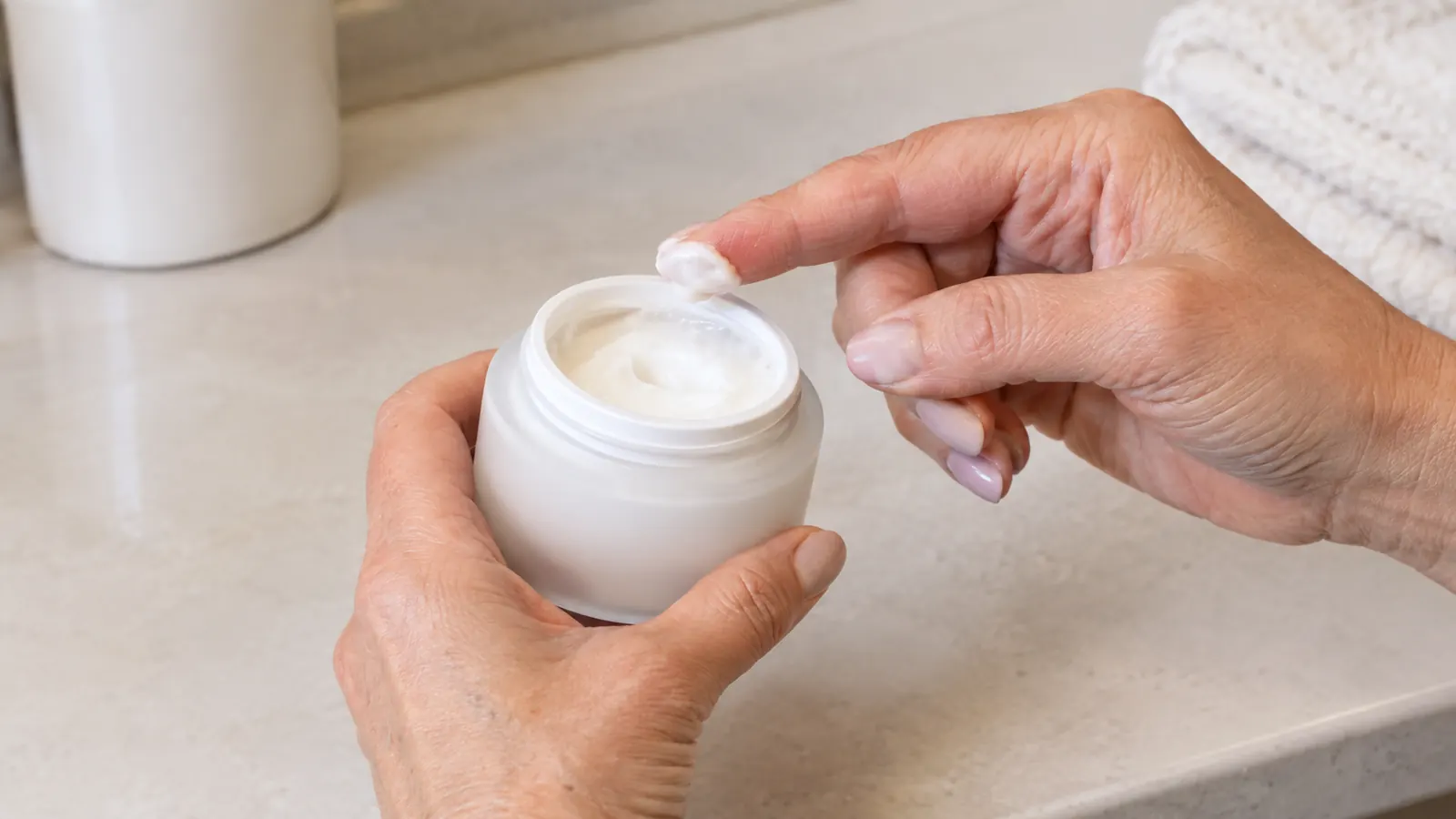 A hand scooping a small amount of night cream from an open jar